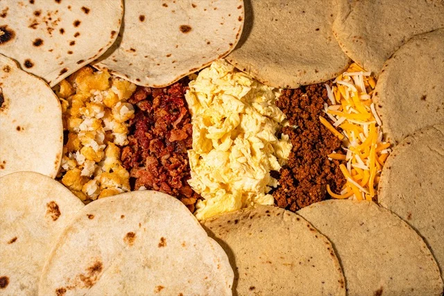 A vibrant spread of Torchy's Tacos breakfast items, including Migas, Wrangler, and Bacon, Egg & Cheese tacos, with fresh ingredients and sauces.